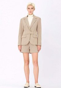 Blazer à carreaux beige avec un design croisé, associé à un short assorti. Présente une texture lisse et une coupe structurée.