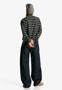 Pulóver je vyrobený z tmavosivého materiálu s bielymi horizontálnymi pruhmi, má dlhé rukávy a pružné manžety. Nosí sa so širokými tmavomodrými džínsami a sivou čiapkou.