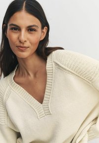 Ebaretsiga heegelknit särk, millel on sügav V-kaelus, tekstuuritud õlad ja soonikdetailid, omades lõtva istuvust ning pehmet ja kerget materjali.