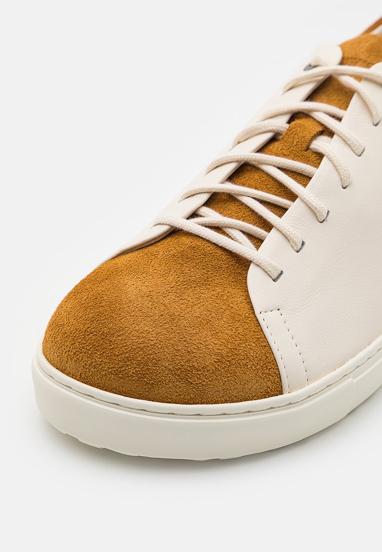Sneaker mit einer sandfarbenen Wildlederkappe und einem weißen Lederoberteil, ausgestattet mit beigen Schnürsenkeln und einer stabilen weißen Gummisohle.