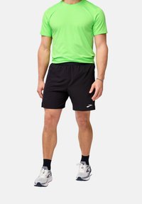 Grön kortärmad tröja för träning och svarta träningsshorts. Skorna är vita med grå detaljer. Tyget verkar vara lätt och ventilerande.