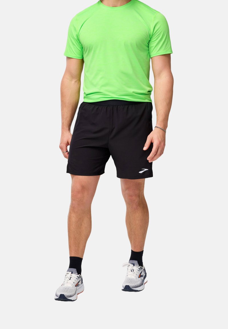 Grön kortärmad tröja för träning och svarta träningsshorts. Skorna är vita med grå detaljer. Tyget verkar vara lätt och ventilerande.