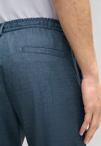 Blauwe joggingsbroek heeft een gemêleerde stof, een elastische tailleband en een klein achterzakje aan de rechterkant.