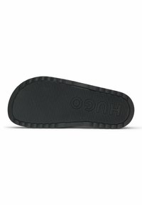 Black rubber shoe sole with a textured grip pattern, featuring prominent ridges and embossed logo. Flat design with slight curvature at the toe.