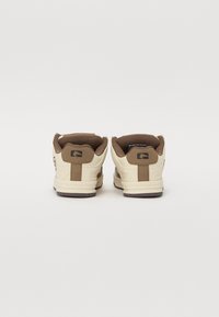 Cream and brown sneakers with a smooth leather upper, padded collar, and textured accents. Rubber sole with a contrasting logo on the heel.