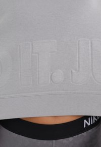 Lichtgrijze cropped sweatshirt met reliëftekst "Just Do It". Heeft een ribbelachtige halslijn en zoom, gecombineerd met zwarte high-waisted leggings.