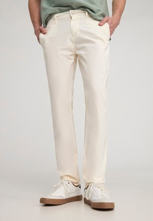 Pantaloni in cotone beige chiaro con taglio dritto, dotati di tasche frontali, passanti per cintura e una texture liscia, abbinati a sneaker bianche.