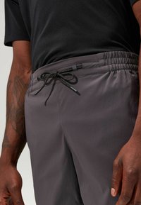 Graue Sportshorts mit elastischem Bund und Kordelzug. Aus glattem Material mit matter Oberfläche und seitlichen Taschen.