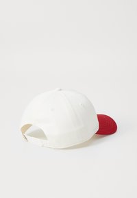 White cotton baseball cap with a red visor, featuring stitching details and an adjustable strap at the back.