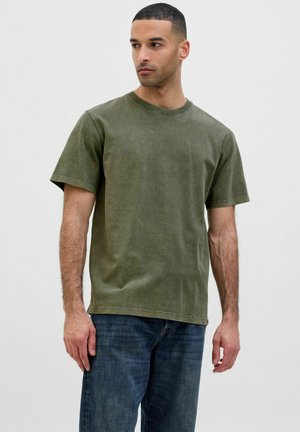 T-shirt en coton vert olive, col rond, manches courtes, coupe décontractée, texture délavée, associé à un jean en denim foncé.