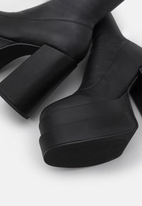 Paire de bottines noires à plateformes avec talons blocs épais et coutures visibles sur des dessus en cuir lisse.