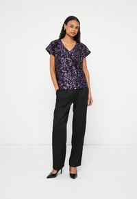 Glitrede lilla paliet-top med V-udskæring og kapperslermer, kombineret med sorte bukser med høj talje og spidse sorte hæle.