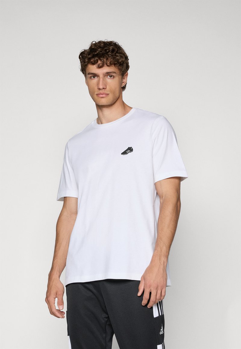 Hvid bomulds t-shirt med rund hals og korte ærmer, der har et lille sort sneaker-graphic på venstre brystområde.