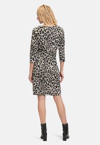 Leopardenmusterkleid mit Dreiviertelärmeln, taillierter Silhouette und knielanger Saum. Der Stoff wirkt weich, kombiniert mit schwarzen Knöchelstiefeln.