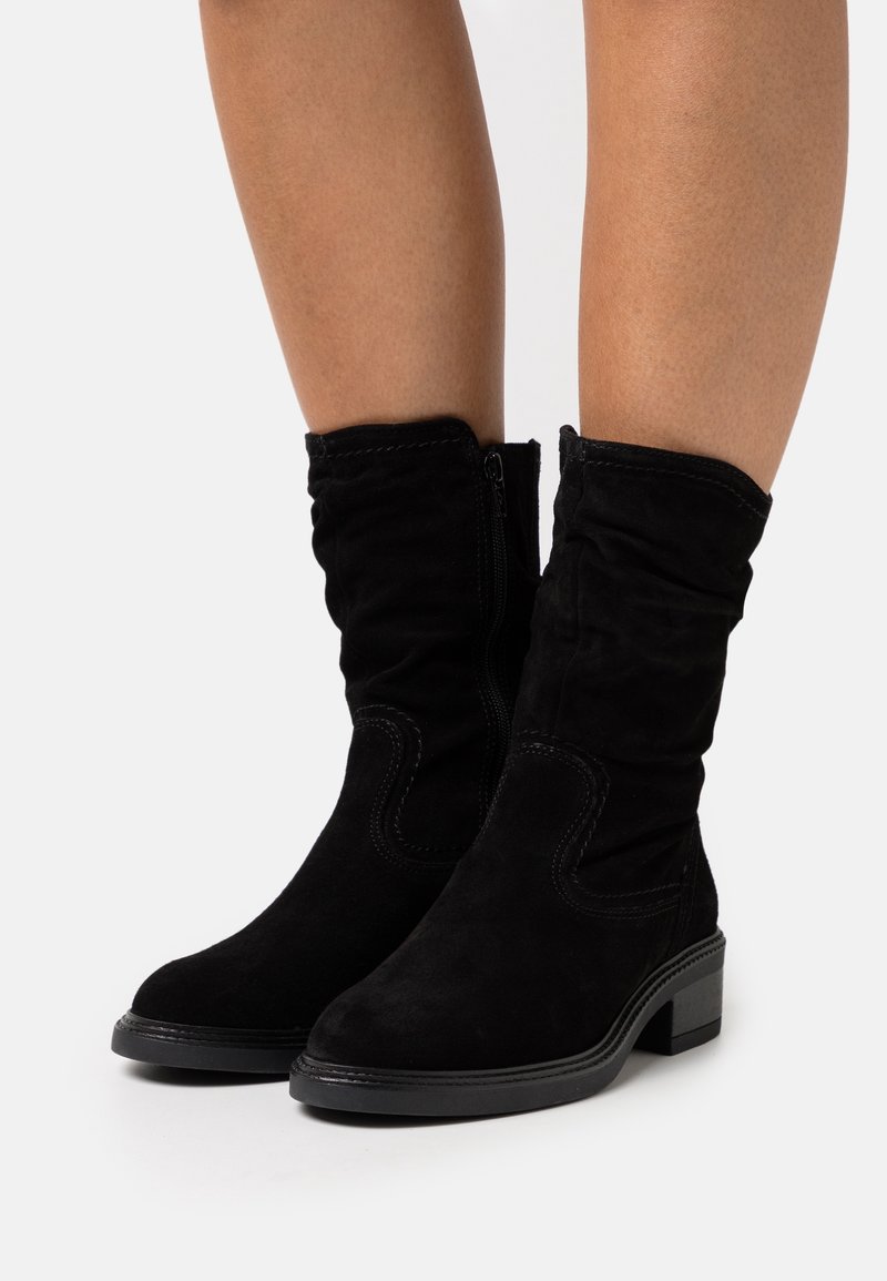 Bottes cheville en daim noir avec un design décontracté, fermeture éclair, petit talon carré et surpiqûres contrastantes.