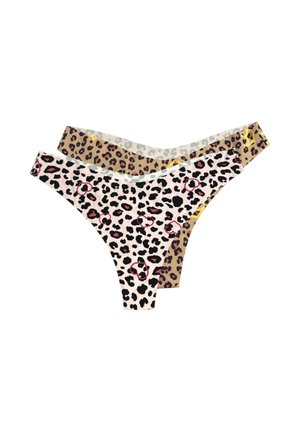 Uśmiechnięta kobieta z blond włosami upiętymi w kok, ubrana w białą krótką koszulkę i różowe majtki w panterkę, chodząca boso na jednolitym tle.