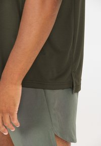 Olivengroene, getextureerde shirt met korte mouwen en split aan de zijkant, gecombineerd met bijpassende groene shorts met een zijsplit voor extra bewegingsvrijheid.
