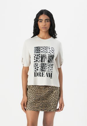 Light beige short-sleeve t-shirt featuring a leopard print graphic and "DREAM BIG" text. Paired with a patterned leopard print skirt.