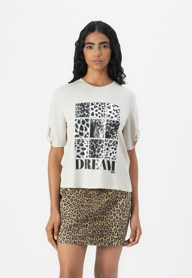 Light beige short-sleeve t-shirt featuring a leopard print graphic and "DREAM BIG" text. Paired with a patterned leopard print skirt.