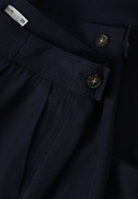 Pantalones navy con diseño de frente plisado, que cuentan con un cierre de botón y una tela texturizada. Etiqueta de tamaño: 38. Incluye dos botones en la cintura.