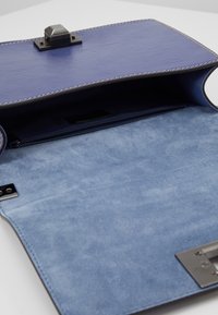 Interno di una borsa a mano in pelle blu con finitura liscia, texture sottile, tasca con zip e chiusura hardware sicura.