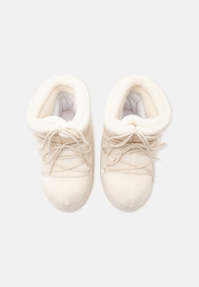 Paire de bottes d'hiver blanches avec une doublure douce et moelleuse, des lacets à l'avant et des bouts arrondis, vues de dessus sur un fond uni.