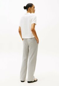 Witte polo met korte mouwen en lichtgrijze sweatpants met zakken. De outfit heeft een relaxed fit en zachte texturen, geschikt voor casual draag.