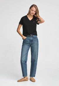 Svart v-ringad t-shirt med kort ärm, tillsammans med högmidjade blå denimjeans och tan loafers, som visar en avslappnad passform och rena linjer.