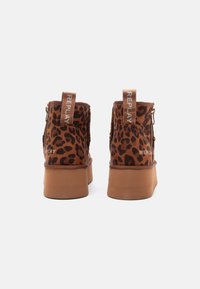Een paar bruine enkelboots met luipaardprint en platform, met zijritsen en het "REPLAY" logo op de hieltabs, getoond vanuit de achterkant.