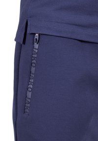 Shorts de sport bleu marine avec une poche zippée sur le côté ornée d'un motif de logo discret, tissu doux et un léger fente au bas.