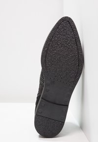 Zapato negro texturizado con parte superior tejida y suela de goma sólida que presenta un diseño estampado y acentos de agarre circular. Talla 37.