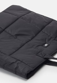 Czarna pikowana torba z materiału o gładkiej teksturze, z małą metką marki oraz podwójnymi uchwytami do noszenia. Lekka i wyściełana konstrukcja.