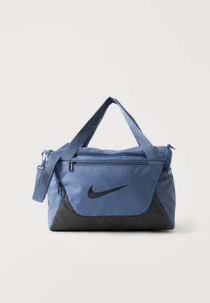 Μπλε και μαύρη τσάντα τύπου duffel Nike με διπλές λαβές, ιμάντα ώμου, μπροστινή τσέπη με φερμουάρ και πλαϊνές θήκες από δίχτυ σε απλό φόντο.