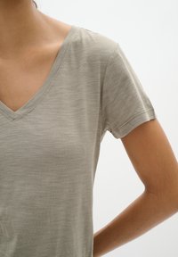  Lichtgrijze V-hals t-shirt in een zachte, gestructureerde stof met korte mouwen. De halslijn en de randen van de mouwen hebben subtiele stikdetails.