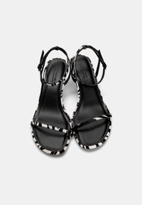 Sandales à talons hauts noir et blanc avec un motif imprimé zèbre, dotées de fines brides et d'une semelle intérieure noire mate et lisse.