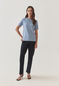 Světle modrý top s krátkým rukávem, kulatým výstřihem, v kombinaci s navy elegantními kalhotami a černými sandály na podpatku. Hladká tkanina, přiléhavý střih.