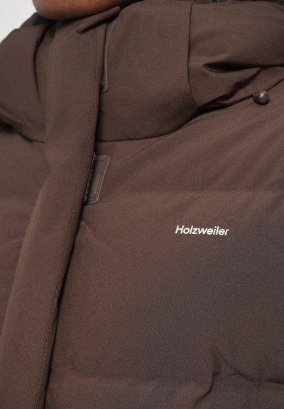 Pruun polsterdatud jakk Holzweileri logoga rinna piirkonnas ja nähtavate õmbluse detailidega.