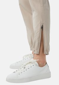 Pantalons beiges fuselés avec des zips aux chevilles, assortis à des baskets en cuir blanches avec des orteils ronds et des semelles plates.