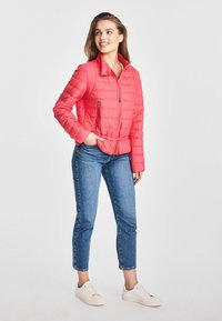 Czerwona ocieplana kurtka z pikowanym wzorem, z zamkami błyskawicznymi w kieszeniach i sznurkiem w pasie. Połączona z niebieskimi dżinsami i białymi trampkami.