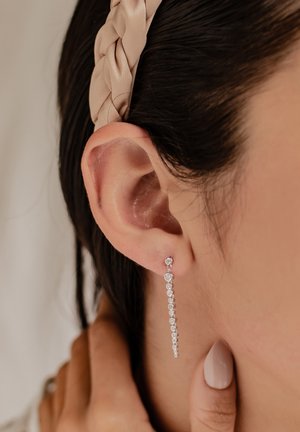 Silberne schwebende Ohrringe mit einem linearen Design, das mehrere kreisförmige klare Edelsteine zeigt und auf der Haut einen eleganten, modernen Look verleiht.