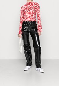 Röd och vit mönstrad långärmad topp med hög hals, tillsammans med svarta glänsande högmidjade byxor och vita sneakers. Vit handväska.