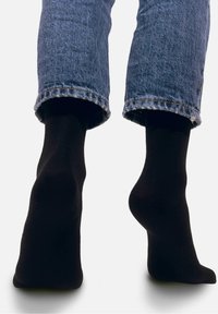 Czarne bawełniane skarpetki noszone z podwiniętymi dżinsami, o gładkiej fakturze i prostym wzorze, podkreślające komfort i dopasowanie.