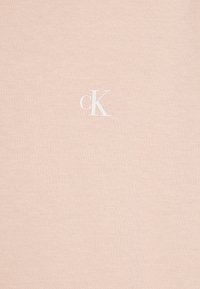 Světle růžové bavlněné tričko s malým bílým logem "cK" na dolním levém okraji. Jemná textura s klasickým designem výstřihu do srdce.