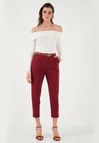 Top bianco a coste, off-the-shoulder, abbinato a pantaloni rossi a vita alta e cropped con cintura marrone e sandali marroni con punta aperta.
