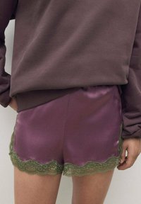 Pantalones cortos de satén en púrpura profundo con un borde de encaje verde en forma de concha. Cintura elástica, textura suave y corte relajado.