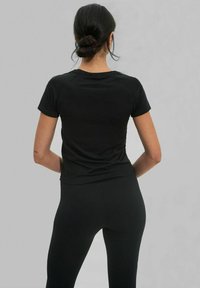 Haut noir à manches courtes ajusté avec un col rond et une texture lisse, assorti de leggings noirs. Design minimaliste sans logos visibles.