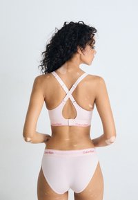 Lichtroze beha met gekruiste banden en het Calvin Klein-logo in het rood op de band, gecombineerd met bijpassende bikini slips. Gladde stofstructuur.