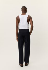 Μαύρο παντελόνι με ίσια γραμμή, συνδυασμένο με λευκό τοπ, ορατές πίσω τσέπες, φορεμένο με καφέ παπούτσια, μινιμαλιστικός σχεδιασμός.