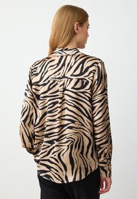 Satin shirt met een tan achtergrond en gedurfde zwarte tijgerstrepen, lange mouwen, een puntige kraag en een rugdetail.