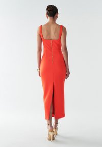 Oranje fitted jurk met een vierkante achterkant, ritssluiting detail en een hoge split tot boven de dij. Gladde stof met brede banden en midi-lengte.